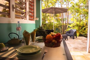 A dining table with plates, cutlery, a water bottle, and a fruit basket. - T1 D'ALICE CLASS 2* 1.2 KM FROM BOURG BEACH (SAINTE ANNE)