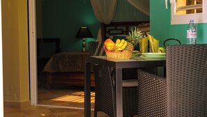 A room with a bed, a table with fruit, wicker chairs, a lamp, and a window with curtains. - T1 D'ALICE CLASS 2* 1.2 KM FROM BOURG BEACH (SAINTE ANNE)