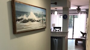A hallway with a wooden floor, a painting of waves on the wall, a ceiling fan, and a view into a dining area. - Fully remodeled, block to beach. 2-story, first floor entry, park at front door (Hilton Head Island)