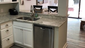 A kitchen with a dishwasher, a sink, and a countertop. There are cabinets, a clock, and a decorative paddle on the wall. - Fully remodeled, block to beach. 2-story, first floor entry, park at front door (Hilton Head Island)
