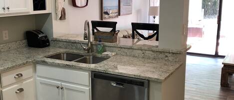 A kitchen with a dishwasher, a sink, and a countertop. There are cabinets, a clock, and a decorative paddle on the wall.