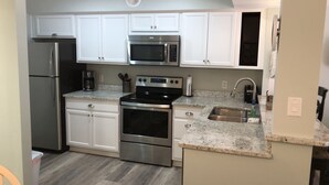 A modern kitchen with stainless steel appliances, white cabinetry, and a granite countertop. - Fully remodeled, block to beach. 2-story, first floor entry, park at front door (Hilton Head Island)