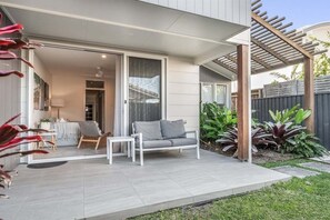 Un patio moderno con un divano grigio, un tavolino e una sedia bianca. Si apre una porta scorrevole in vetro su uno spazio interno con una ventola a soffitto.