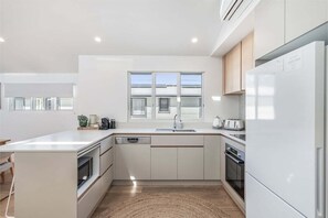 Una cucina moderna con mobili bianchi, forno a incasso, lavastoviglie e un grande frigorifero.
