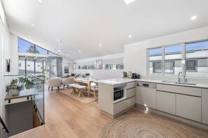 A modern kitchen with a dining area, large windows, and a view of the outside. - From the minute you walk in the front door you will be in awe of the styling. (Lennox Head)