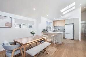 A modern kitchen with a central island, wooden dining table, and bar stools. - From the minute you walk in the front door you will be in awe of the styling. (Lennox Head)