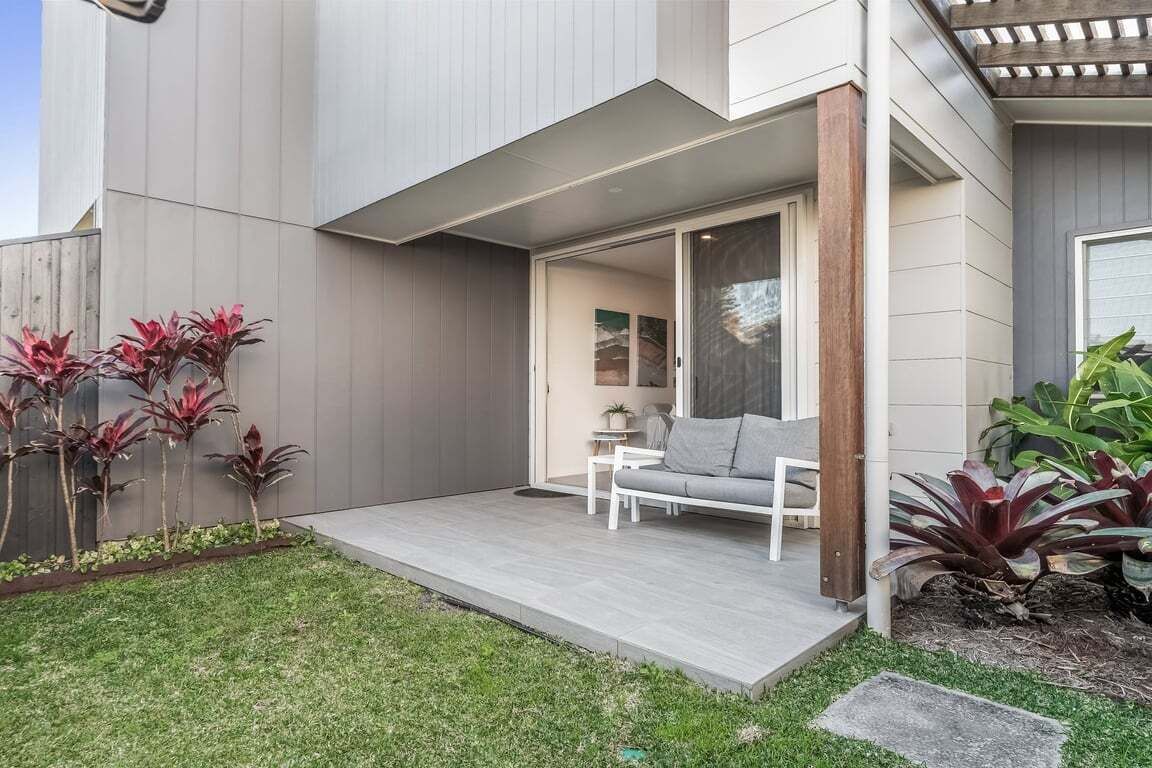 A modern house with a covered patio, a grey exterior, and a small garden with red-leafed plants.