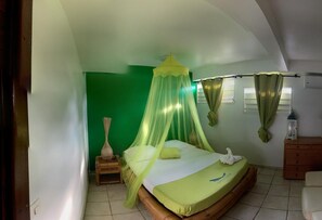 A bedroom with a green wall, a bed with a canopy, a wooden nightstand, a small table, and a dresser.