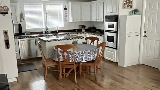 Une cuisine moderne avec des meubles blancs, une table à manger avec des chaises et un plancher en bois.