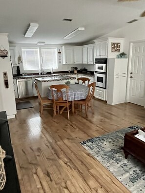 Une cuisine moderne avec des meubles blancs, une table à manger avec des chaises et un plancher en bois.