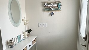 Une salle de bain avec un meuble-lavabo blanc, un tapis à motif d’étoile de mer et une pancarte « Beach House » accrochée au mur.