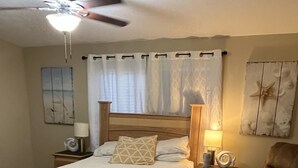 Une chambre à coucher comprenant un lit, une chaise, une table de chevet, une lampe et un ventilateur de plafond.