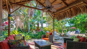 An outdoor patio with wicker furniture, a stone table, and a thatched roof. - Tiki Hut in tropical paradise (Dunedin)