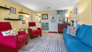 A cozy living room with a red armchair, a blue sofa, and a patterned rug. - Tiki Hut in tropical paradise (Dunedin)