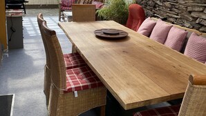 An outdoor dining area with a wooden table, wicker chairs, and a stone wall. - Casa Siepelunga (Villmar)