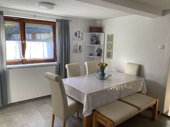 A dining area with a table covered by a white tablecloth, surrounded by four chairs and two benches. - Casa Siepelunga (Villmar)