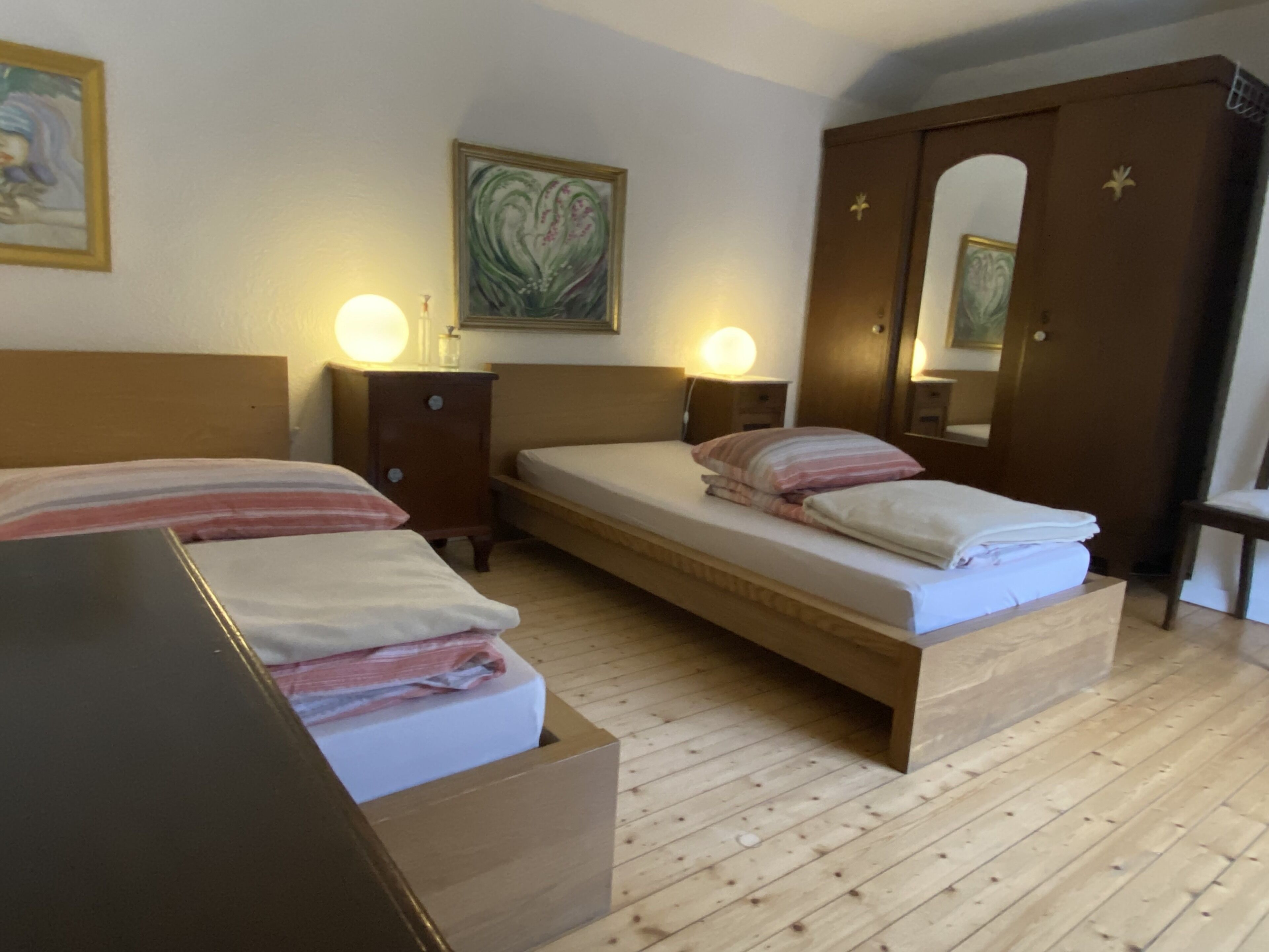 A room with two beds, wooden headboards, a wooden wardrobe, and a mirror.