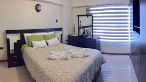 Une chambre d’hôtel avec un lit, une commode, un miroir et une fenêtre avec des stores.