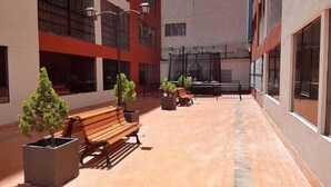 Une cour extérieure agrémentée de bancs et de plantes en pot, entourée de bâtiments dotés de grandes fenêtres et d’un espace de repos abrité.