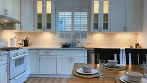 A modern kitchen with white cabinetry, a central island with seating, and a dining area with a wooden table and chairs. - Golf course house with 2 master bedrooms (Fontana)