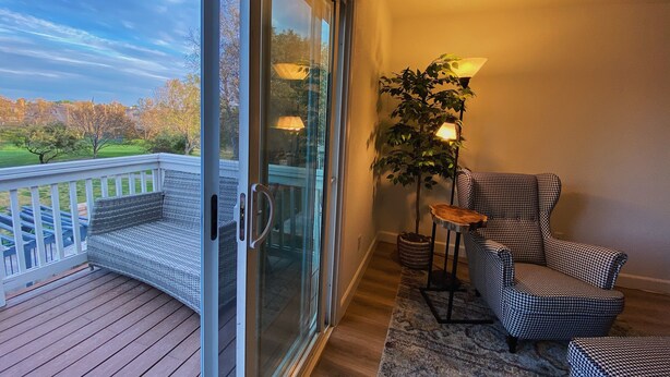 A balcony with a wicker sofa, a houndstooth armchair, a lamp, and a potted plant. - Golf course house with 2 master bedrooms (Fontana)