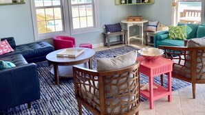 A living room with a blue sofa, a red chair, a wooden coffee table, and a TV mounted on the wall. - Oceanfront Oasis House 5 bedroom, 3.5 bath Elevator - Excellent Reviews (Holly Ridge)