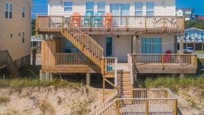 A beachfront building with multiple balconies, wooden staircases, and beach chairs. - Oceanfront Oasis House 5 bedroom, 3.5 bath Elevator - Excellent Reviews (Holly Ridge)