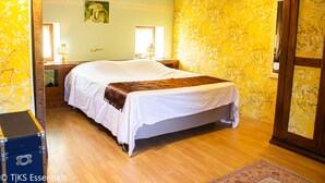 A bedroom with a large bed, wooden floor, floral wallpaper, and a wooden wardrobe. - Pleasures and Idleness... (Boisredon)