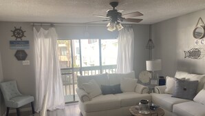 A living room with a white sofa, a round coffee table, and a ceiling fan. - Private condo next to state park and pier-now booking for summer! (Gulf Shores)