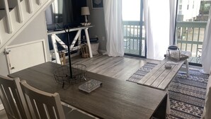 A dining area with a wooden table, chairs, and a view of the outside balcony. - Private condo next to state park and pier-now booking for summer! (Gulf Shores)