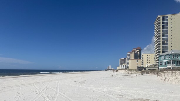 A beach with footprints leading to a building with multiple floors and balconies. - Private condo next to state park and pier-now booking for summer! (Gulf Shores)