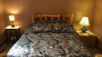 A bed with a camouflage-patterned bedspread, two bedside lamps, a wooden headboard, and a small table with a lamp and a book.