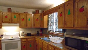 Une cuisine avec des meubles en bois, une cuisinière, un four à micro-ondes et une fenêtre donnant sur les arbres.