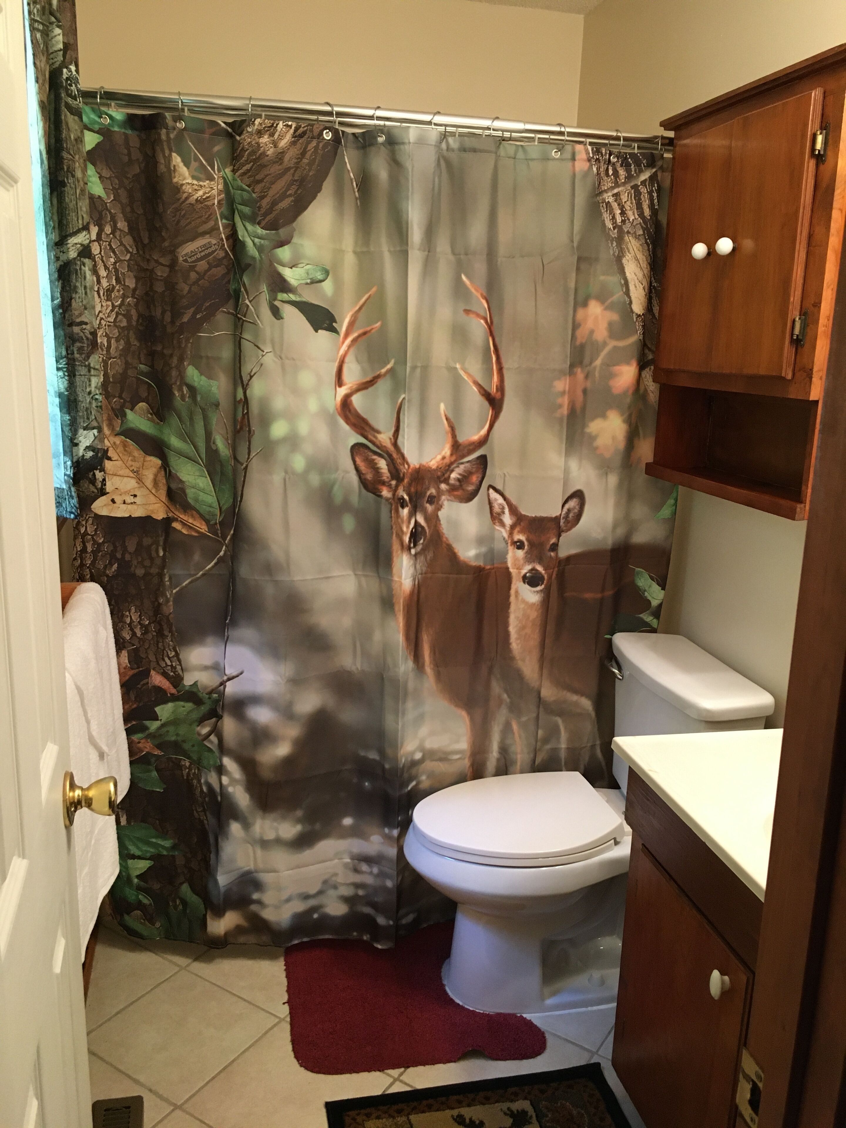 A bathroom with a deer-themed shower curtain, a toilet, and a wooden cabinet.