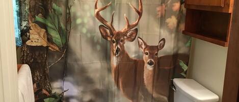 A bathroom with a deer-themed shower curtain, a toilet, and a wooden cabinet.