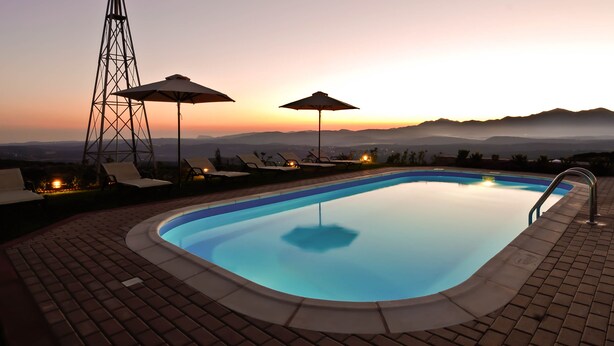 A swimming pool with lounge chairs and umbrellas, surrounded by mountains and a sunset. - Luxurious Panoramic View Villa (Archanes-Asterousia)