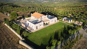 A modern house with solar panels, a spacious lawn, and olive groves in the background. - Luxurious Panoramic View Villa (Archanes-Asterousia)