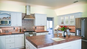 Une cuisine moderne avec des meubles blancs, un îlot central, un réfrigérateur en acier inoxydable et un mur de fond en briques.