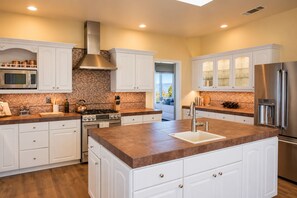 A modern kitchen with white cabinetry, a central island, stainless steel appliances, and a view to the outdoors.