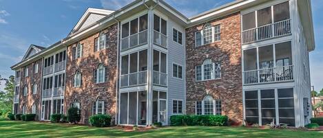 A multi-story building with a brick facade, large windows, and a well-maintained lawn.