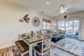 A dining area with a wooden table set for four, surrounded by white chairs.