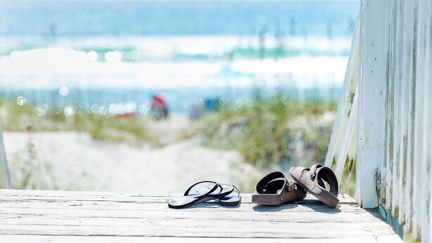 Sandalen auf einem Holzboden mit Blick auf das Meer.