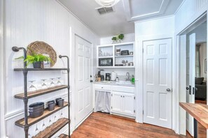 A kitchen with white cabinetry, a wooden floor, and a built-in shelf unit with glassware and kitchen items.
