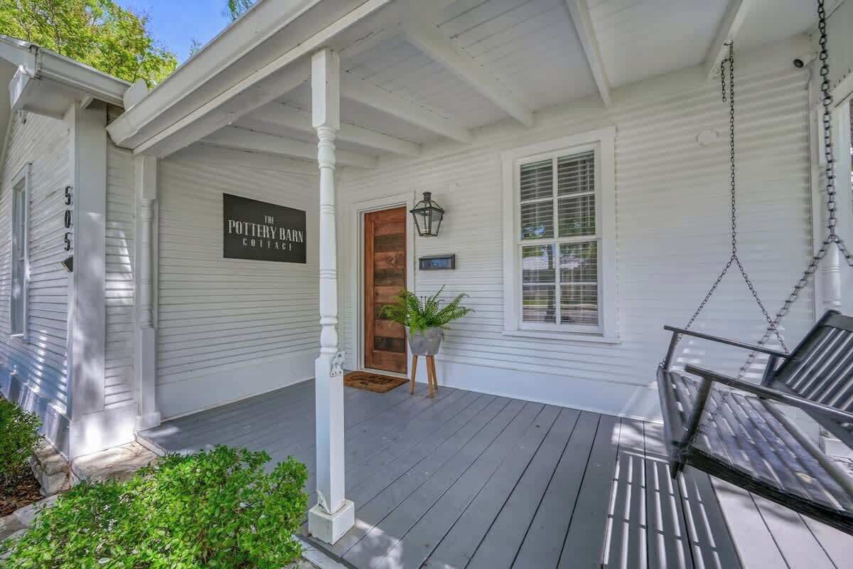 A porch with a swing chair, a potted plant, and a sign reading "The Pottery Barn Cottage."