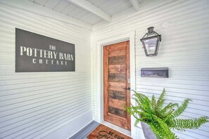 A porch with a sign reading "The Pottery Barn Cottage," a wooden door, a lantern, and a welcome mat.