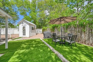 Ein Garten mit einer Terrassentischgruppe, Stühlen und einem überdachten Grillbereich.