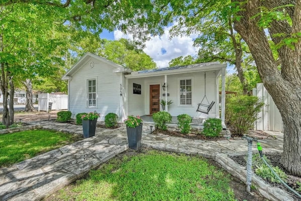 A single-story house with a porch, a mailbox, and a small garden with potted plants.