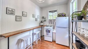 A compact kitchen with white appliances, wooden bar counter, and framed pictures on the wall. - Romantic-Steps To Main-FirePit! (Fredericksburg)