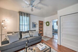 Ein Wohnzimmer mit grauem Sofa, einem Glastisch und einem Deckenventilator.