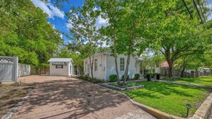 A residential property with a gravel driveway, a small white house, and a well-maintained lawn. - Romantic-Steps To Main-FirePit! (Fredericksburg)